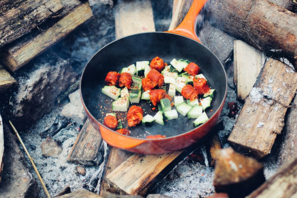 orange skillet with veggies over the campfire